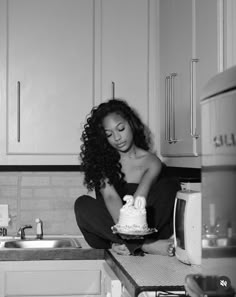 a black and white photo of a woman sitting on the kitchen counter cutting a cake