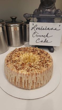 a cake sitting on top of a white plate next to two silver pots and a sign