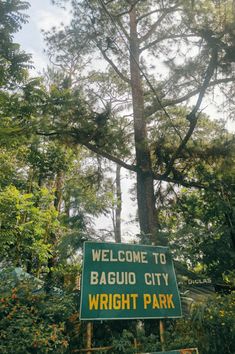 a welcome sign to baguio city wright park in front of some tall trees