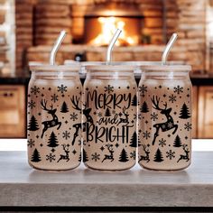 three glass tumblers with merry and bright designs on them sitting in front of a fireplace