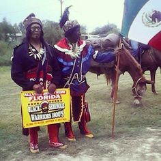 two men dressed in native american garb standing next to each other with flags on their backs