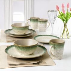 a table set with plates, cups and vases on top of a place mat