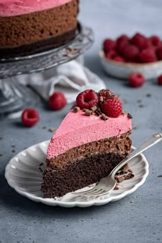 a slice of chocolate cake with raspberries on top and another piece in the background