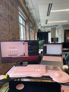 two computer monitors sitting next to each other on top of a pink desk in an office