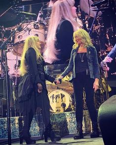 two women shaking hands on stage with drums in the background and one woman standing next to her