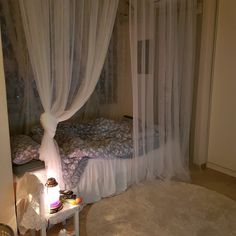 a bedroom with sheer curtains and a bed in the corner next to a night stand