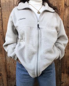 a woman standing in front of a wooden wall wearing a white jacket with the word columbia written on it