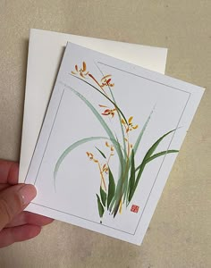 a hand is holding two cards with flowers on them, one has yellow and green leaves