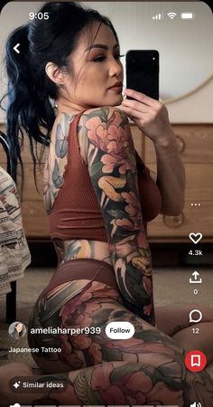 a woman sitting on the floor with tattoos on her arms and leg, holding a cell phone