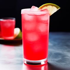 a red drink sitting on top of a table next to a slice of lemon and lime