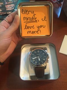 a person holding up a watch in a box with writing on the front and back