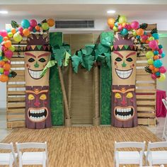 a decorated stage with chairs and balloons on the floor, in front of two large tiki masks