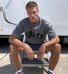 a man sitting on a chair in front of a white trailer with his legs crossed