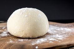 a ball of dough sitting on top of a wooden cutting board covered in powdered sugar