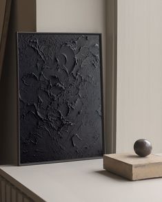 a black painting sitting on top of a white table next to a small stone ball