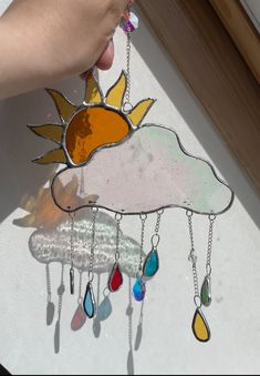 a hand holding onto a stained glass sun and cloud with tears hanging from it