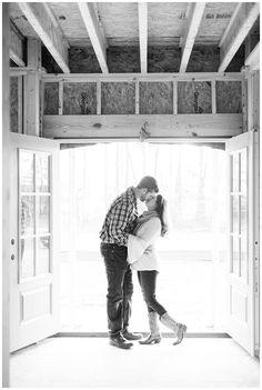 a man and woman kissing in front of an open door with wood framing on the walls