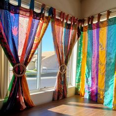 colorful curtains are hanging in front of a window with the sun shining through them and reflecting on the wood floor