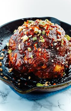 a black plate topped with meat covered in sauce and toppings on top of a marble counter