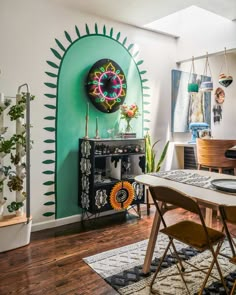 a dining room table and chairs in front of a green wall with art on it