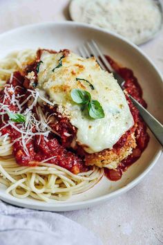 a white bowl filled with pasta and sauce on top of a marble countertop next to a silver fork