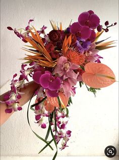 a bouquet of flowers is being held up by someone's hand in front of a white wall