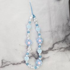 a blue and white beaded necklace sitting on top of a marble table next to a cell phone