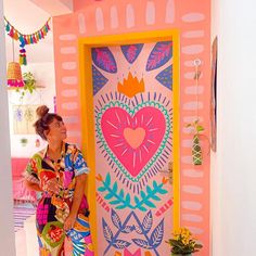 a woman standing in front of a brightly colored door with a heart painted on it