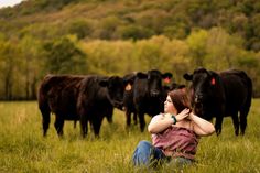 a woman sitting in the grass with cows behind her