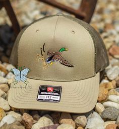 a baseball cap with a duck on it sitting on some rocks and gravel next to a chair