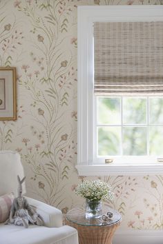 a living room with floral wallpaper and a window in the corner next to a chair