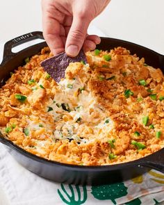 a person dipping a tortilla chip into a skillet filled with chicken and cheese