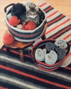 a cat sitting in a basket on top of a rug next to two bowls filled with balls of yarn