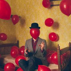 a man sitting on top of a bed surrounded by red balloons in front of him