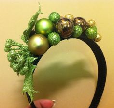 a hand holding a green and gold headband with christmas ornaments on top of it