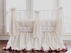 a white crib with pink ruffles and bows on the bed skirt, in front of large windows