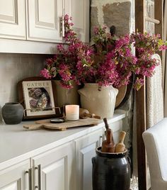 a vase filled with pink flowers sitting on top of a counter next to a candle