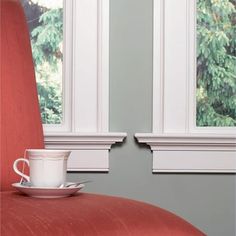 a red chair with a cup and saucer on it in front of two windows