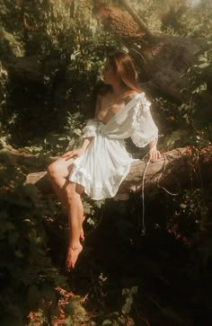 a woman sitting on top of a log in the middle of some bushes and trees