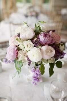 a vase filled with lots of flowers sitting on top of a white tablecloth covered table