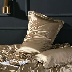 an unmade bed with gold sheets and pillows on top of it next to a lamp