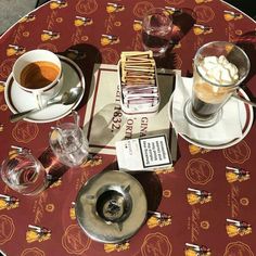 two cups of coffee sit on top of a red tablecloth with an orange and yellow pattern