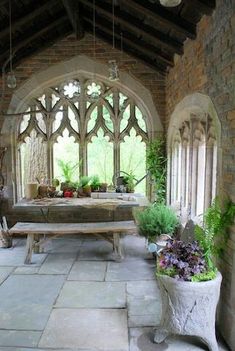 a stone building with an arched window and bench in the center, surrounded by potted plants