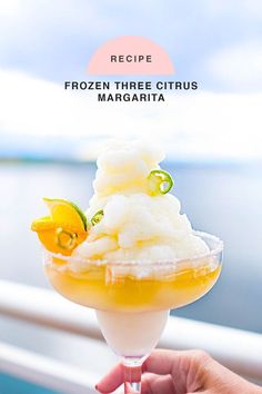 a person holding up a frozen three citrus margarita in front of the ocean with text overlay that reads recipe frozen three citrus margarita