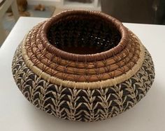 a woven basket sitting on top of a white table next to a black and brown vase