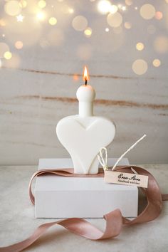 a white heart shaped candle sitting on top of a box with a ribbon around it