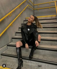 a woman sitting on some stairs with her legs crossed and wearing black boots, looking up at the sky