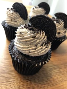 chocolate cupcakes with white frosting and oreo cookies on top sitting on a table