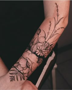 a woman's arm with flowers and leaves tattooed on the wrist, in black and white