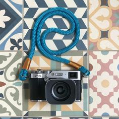 a camera with a blue rope attached to it sitting on a tiled floor next to a wall